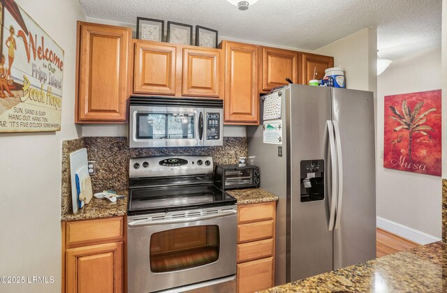 kitchen featuring stainless steel appliances, a textured ceiling, and dark stone countertops