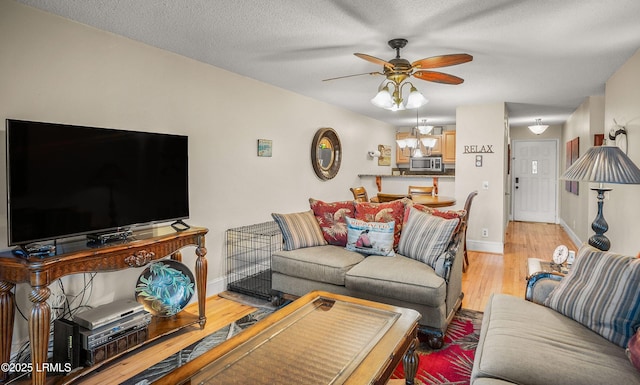 living room featuring ceiling fan, light hardwood / wood-style flooring, and a textured ceiling