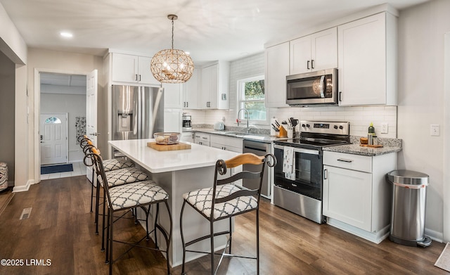 kitchen with a kitchen island, decorative light fixtures, white cabinetry, decorative backsplash, and stainless steel appliances