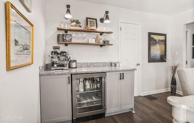 bar featuring dark wood-type flooring, light stone countertops, and beverage cooler