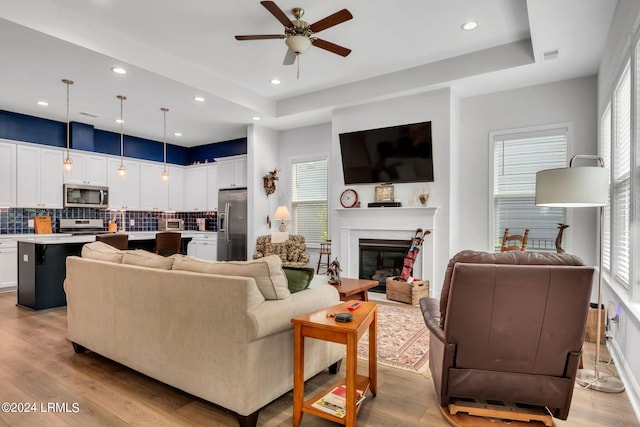 living room featuring a raised ceiling, ceiling fan, and light hardwood / wood-style floors