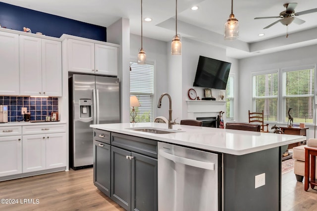 kitchen with sink, hanging light fixtures, stainless steel appliances, an island with sink, and white cabinets