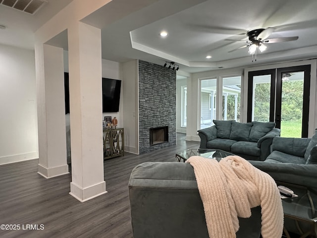 living area featuring a tray ceiling, dark wood finished floors, visible vents, a stone fireplace, and baseboards