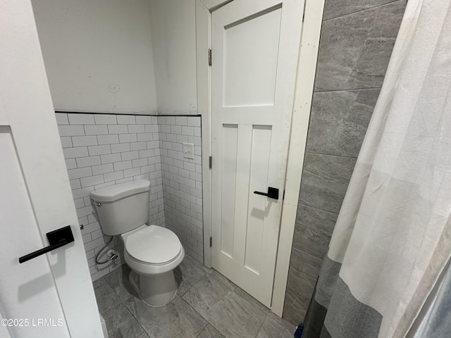 bathroom featuring a wainscoted wall, tile walls, and toilet