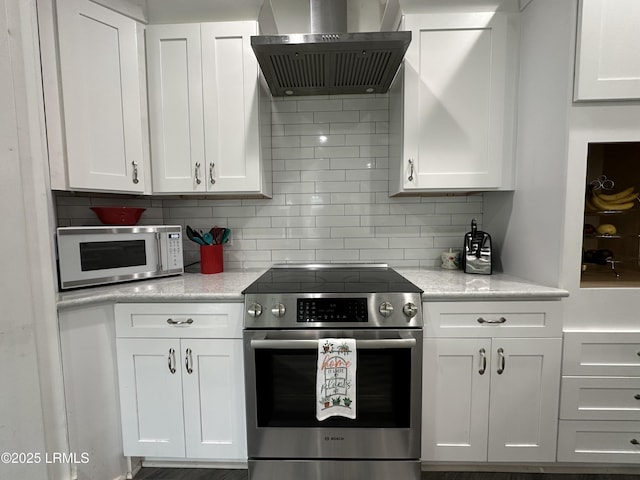 kitchen with white cabinets, wall chimney range hood, white microwave, and stainless steel range with electric cooktop