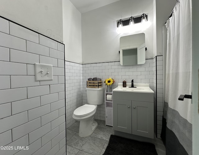 bathroom featuring toilet, a wainscoted wall, vanity, and tile walls