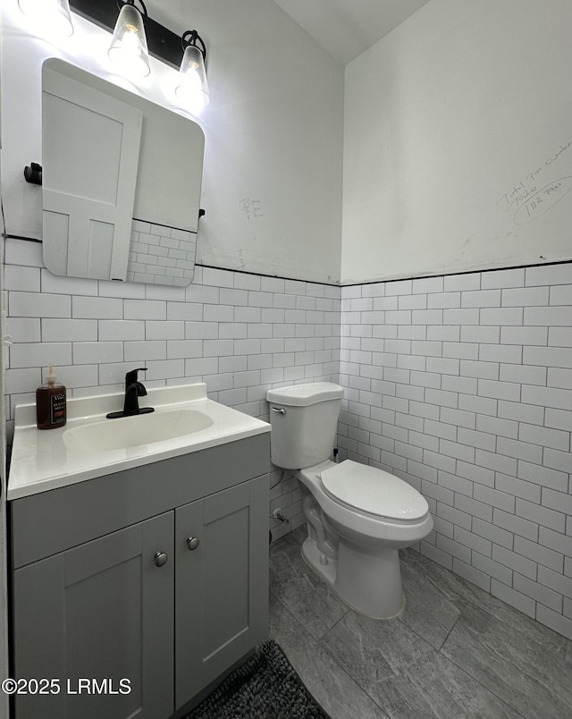 half bathroom featuring tile walls, a wainscoted wall, vanity, and toilet