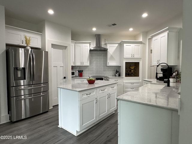 kitchen with visible vents, white cabinets, a kitchen island, stainless steel appliances, and wall chimney range hood