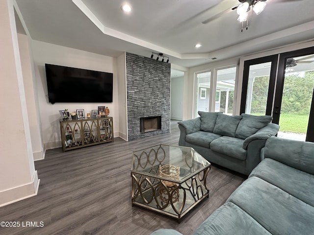 living area featuring dark wood-type flooring, a fireplace, a raised ceiling, and baseboards