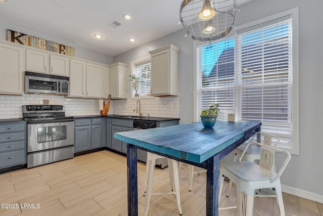 kitchen with pendant lighting, sink, gray cabinetry, backsplash, and stainless steel appliances