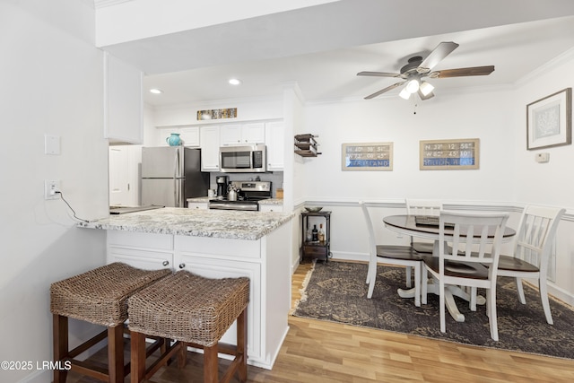 kitchen with appliances with stainless steel finishes, ornamental molding, white cabinets, wood finished floors, and a peninsula