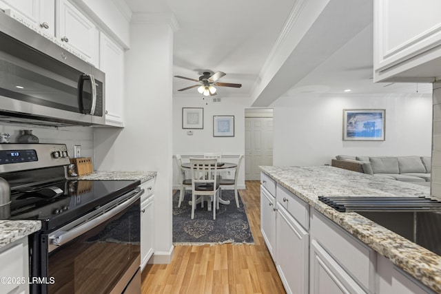 kitchen with ceiling fan, stainless steel appliances, white cabinetry, ornamental molding, and light wood-type flooring