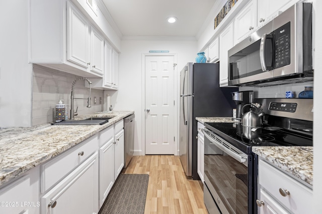 kitchen featuring light wood-style flooring, appliances with stainless steel finishes, ornamental molding, white cabinets, and a sink