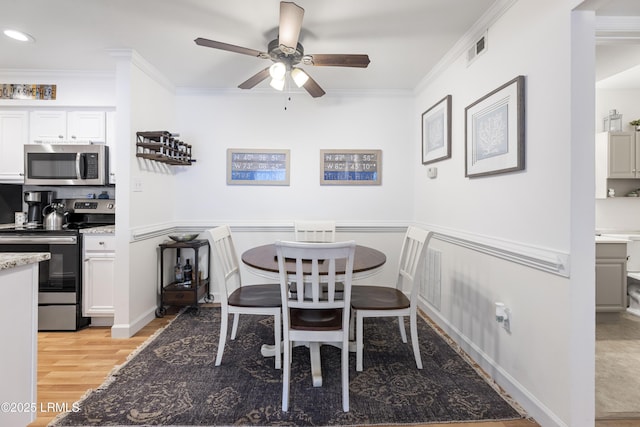 dining room with light wood-type flooring, visible vents, a ceiling fan, and ornamental molding