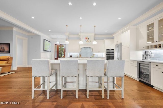 kitchen with wine cooler, white cabinetry, decorative light fixtures, and an island with sink