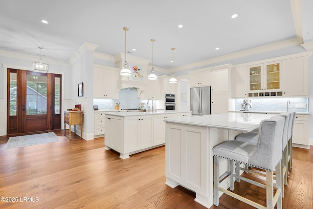 kitchen featuring appliances with stainless steel finishes, white cabinets, backsplash, hanging light fixtures, and a center island