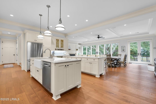 kitchen with a kitchen island with sink, hanging light fixtures, white cabinetry, stainless steel appliances, and beamed ceiling