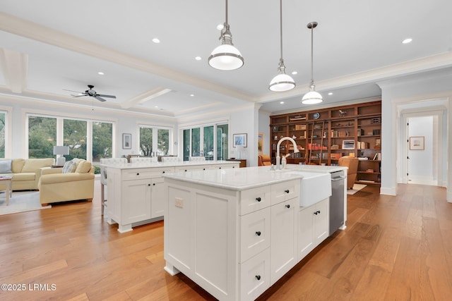 kitchen featuring sink, white cabinetry, hanging light fixtures, beam ceiling, and a kitchen island with sink