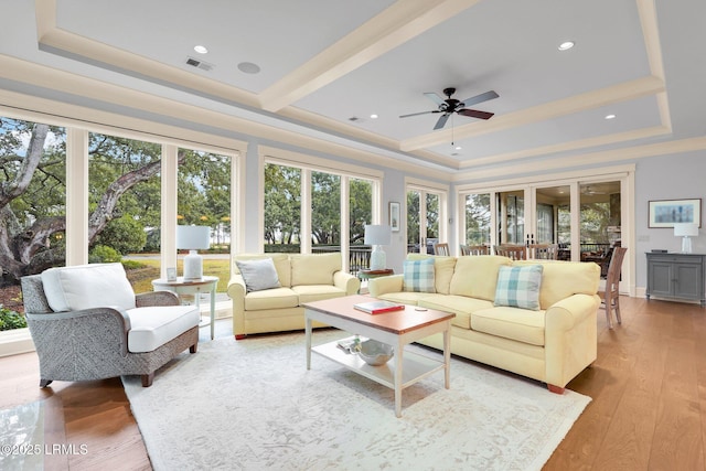 living room with a tray ceiling, ceiling fan, and light wood-type flooring