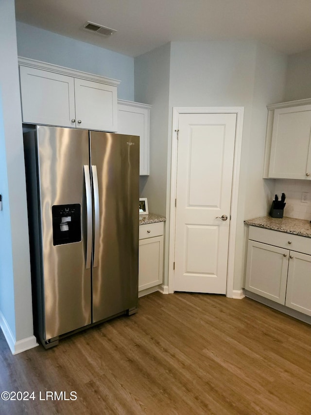 kitchen featuring tasteful backsplash, white cabinets, stainless steel fridge, hardwood / wood-style flooring, and light stone counters