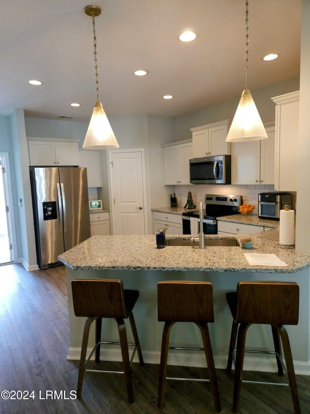 kitchen featuring stainless steel appliances, white cabinetry, a kitchen breakfast bar, and decorative light fixtures