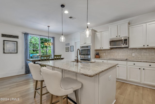 kitchen featuring hanging light fixtures, stainless steel appliances, tasteful backsplash, an island with sink, and white cabinets