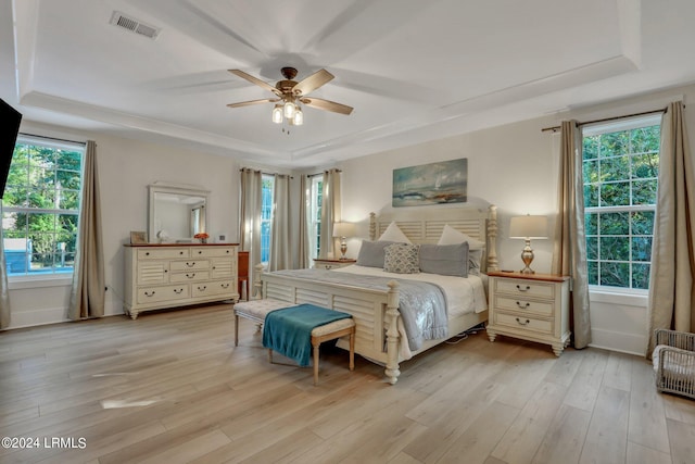 bedroom with light hardwood / wood-style flooring, a raised ceiling, and ceiling fan