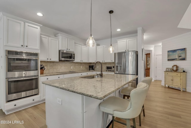 kitchen with pendant lighting, sink, white cabinetry, stainless steel appliances, and light stone countertops