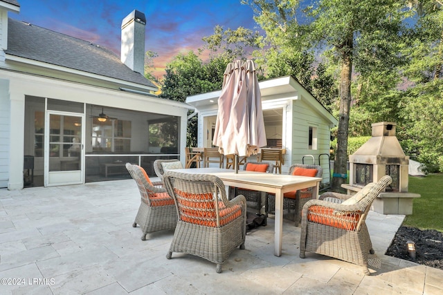 patio terrace at dusk featuring a multi sided fireplace and a sunroom