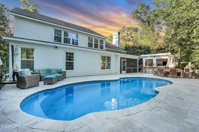 pool at dusk with an outdoor bar, a sunroom, a patio, and an outdoor living space with a fireplace