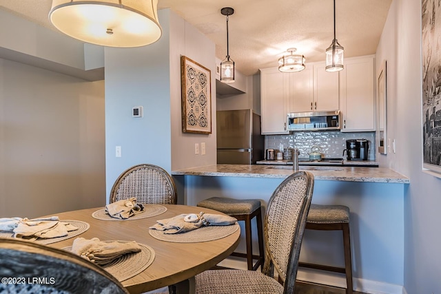 kitchen with white cabinetry, stainless steel appliances, decorative light fixtures, and light stone counters