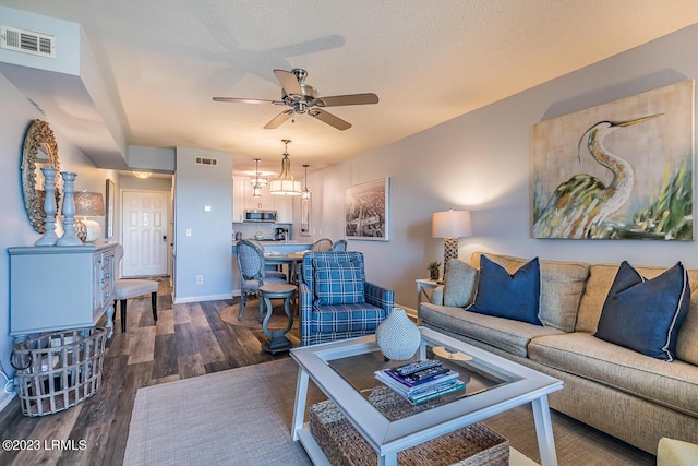 living room featuring dark wood-type flooring, a textured ceiling, and ceiling fan