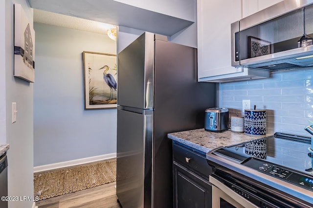 kitchen with tasteful backsplash, white cabinetry, appliances with stainless steel finishes, and light stone counters