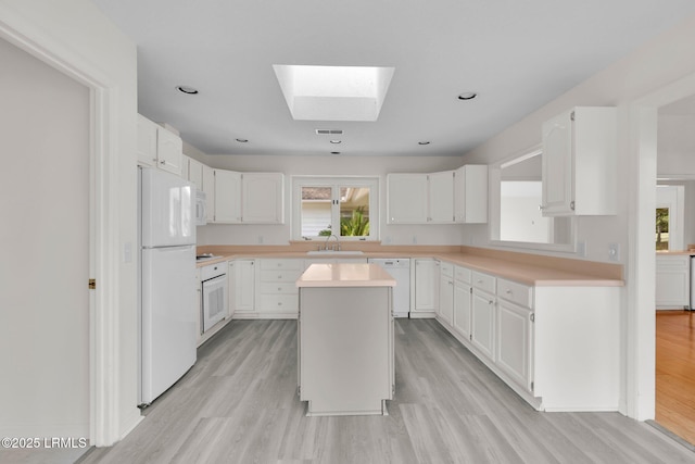 kitchen with light countertops, a skylight, white appliances, and light wood-style flooring