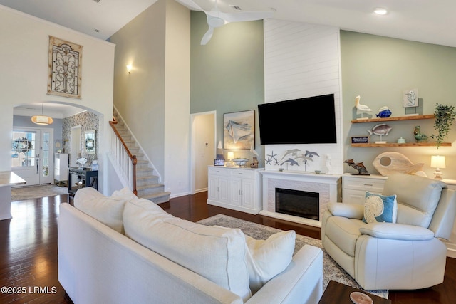 living room featuring high vaulted ceiling, a glass covered fireplace, dark wood finished floors, stairway, and arched walkways