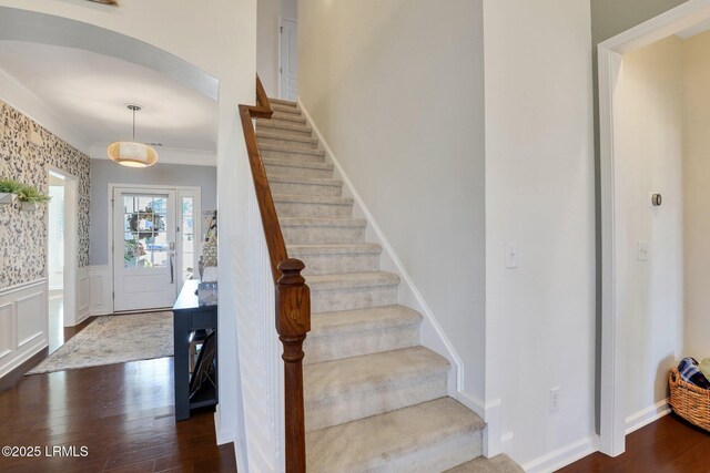 staircase featuring ornamental molding, wainscoting, wood finished floors, arched walkways, and a decorative wall