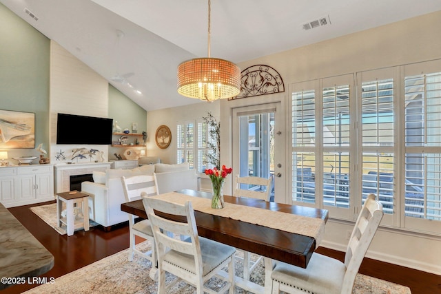 dining room with visible vents, an inviting chandelier, a fireplace, dark wood-style flooring, and vaulted ceiling