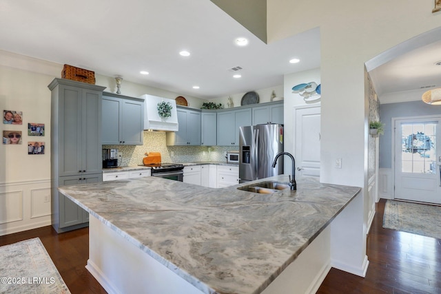 kitchen with a sink, light stone counters, appliances with stainless steel finishes, a peninsula, and wainscoting