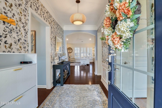 foyer with baseboards, wallpapered walls, arched walkways, dark wood-style flooring, and ornamental molding