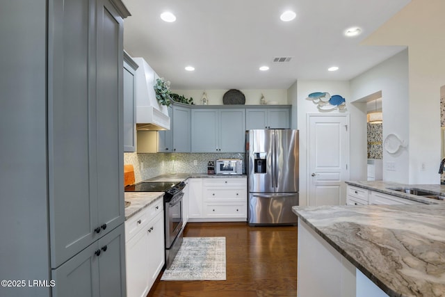 kitchen featuring custom range hood, light stone counters, appliances with stainless steel finishes, and a sink