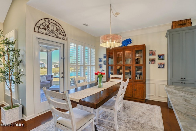 dining area featuring dark wood finished floors, a decorative wall, visible vents, and a wainscoted wall