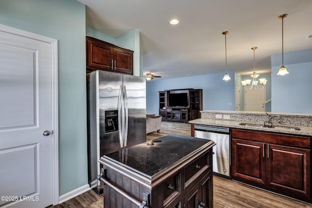 kitchen featuring stainless steel appliances, wood finished floors, a sink, light stone countertops, and decorative light fixtures