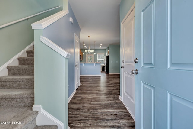 interior space featuring dark wood-style flooring, a notable chandelier, baseboards, and stairs