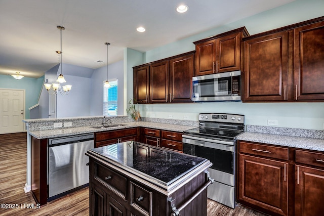 kitchen featuring light stone counters, dark wood-style floors, stainless steel appliances, a sink, and a peninsula