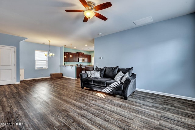 living room with dark wood-style floors, ceiling fan with notable chandelier, visible vents, and baseboards