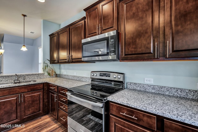 kitchen featuring stainless steel appliances, a sink, dark brown cabinets, and wood finished floors