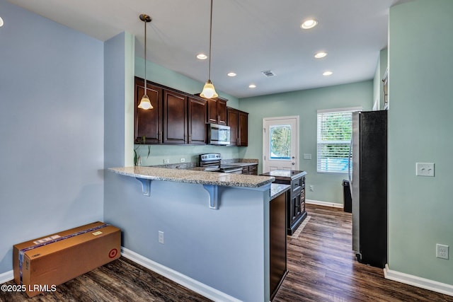 kitchen featuring dark wood-style floors, a breakfast bar area, stainless steel appliances, visible vents, and a peninsula