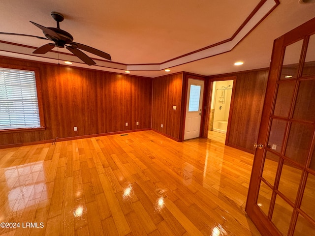 empty room featuring ceiling fan, light hardwood / wood-style floors, and wood walls