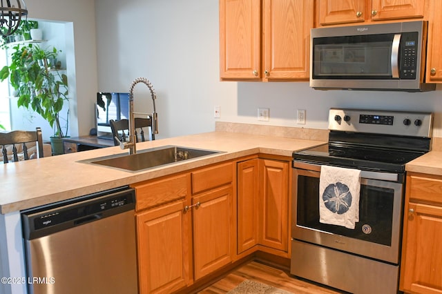 kitchen with appliances with stainless steel finishes, kitchen peninsula, sink, and light hardwood / wood-style flooring