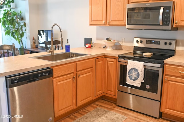 kitchen featuring sink, light hardwood / wood-style flooring, kitchen peninsula, and appliances with stainless steel finishes